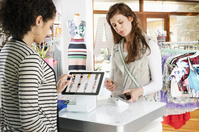 Woman shopping in clothing store paying with smart phone